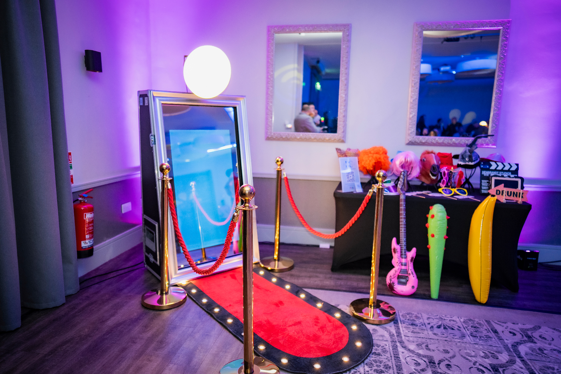 Mirror booth with red carpet, gold posts and prop table under purple lighting