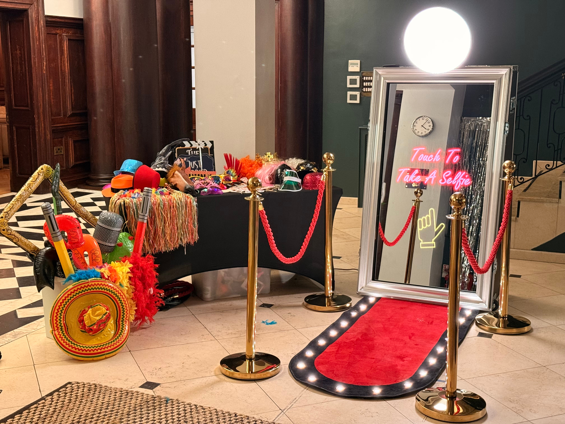 Silver-framed mirror booth with neon 'Touch To Take A Selfie' prompt and prop table