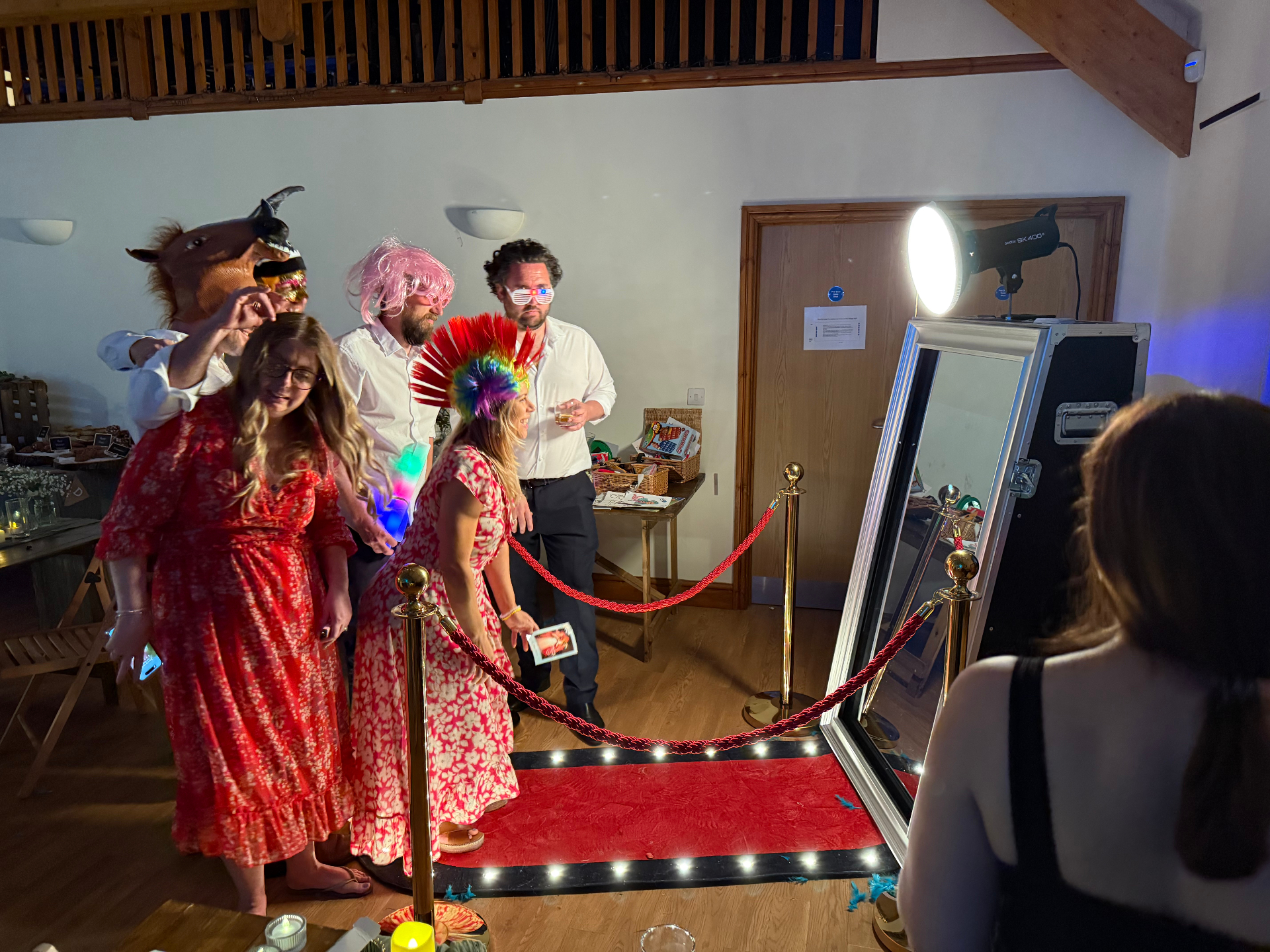 Wedding guests in wigs, horse mask and props posing at the mirror booth in a barn venue